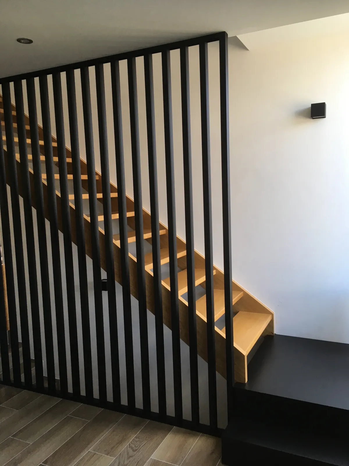 Claustra noir à lattes verticales devant un escalier en bois