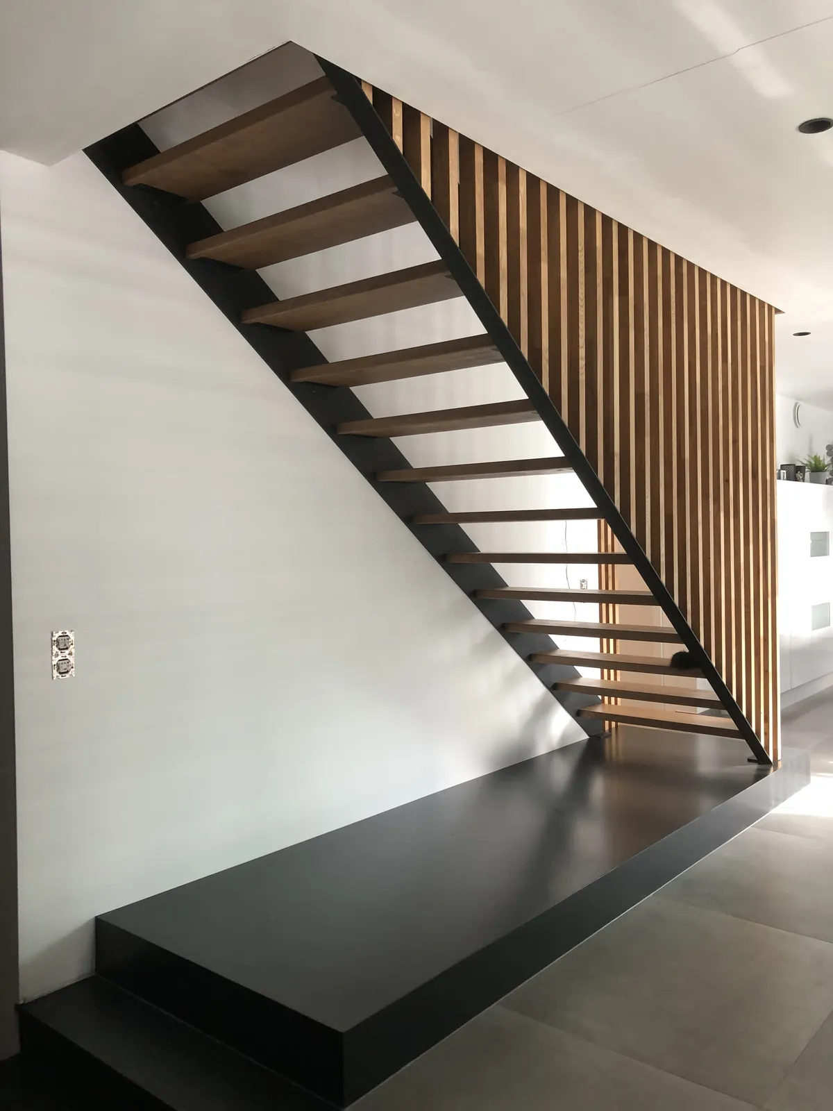 Escalier à limon noir et marches en bois derrière un claustra en lattes