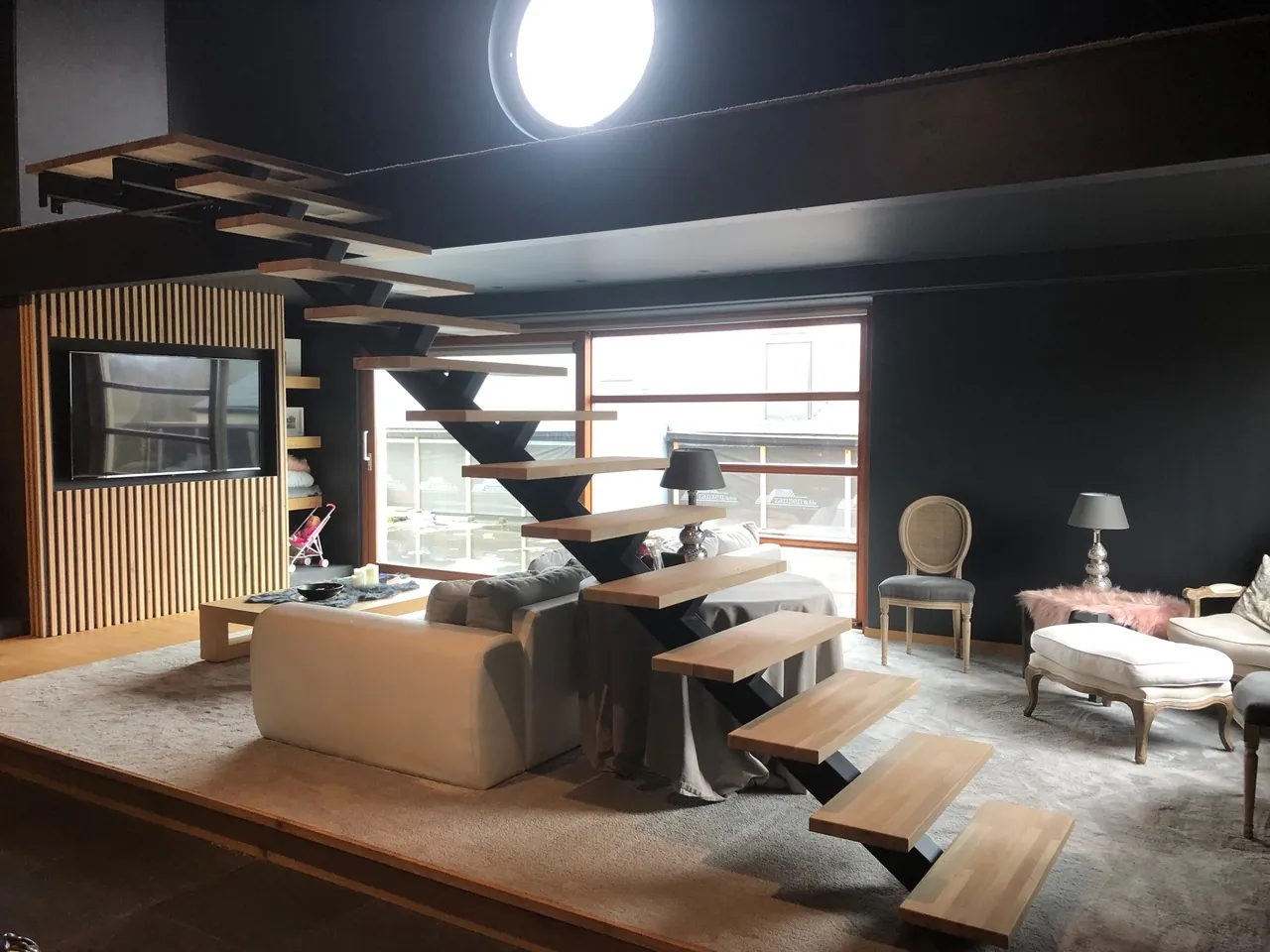 Escalier suspendu à marches en bois dans un grand salon sombre