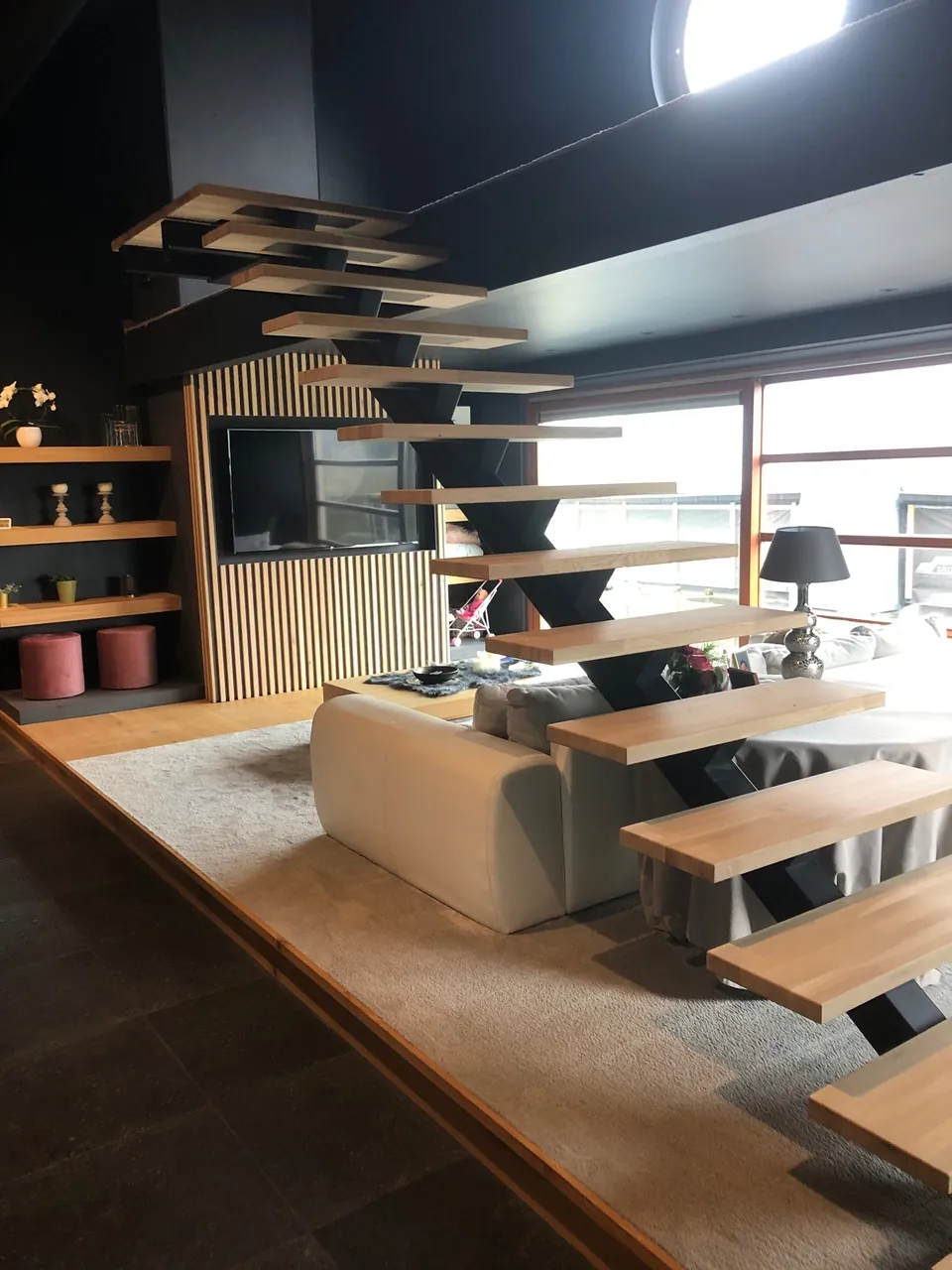 Escalier suspendu en bois clair devant un meuble TV en lattes