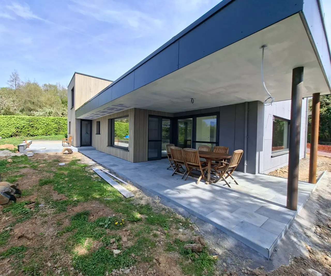 Façade mêlant bardage bois et panneaux gris, sous un large auvent