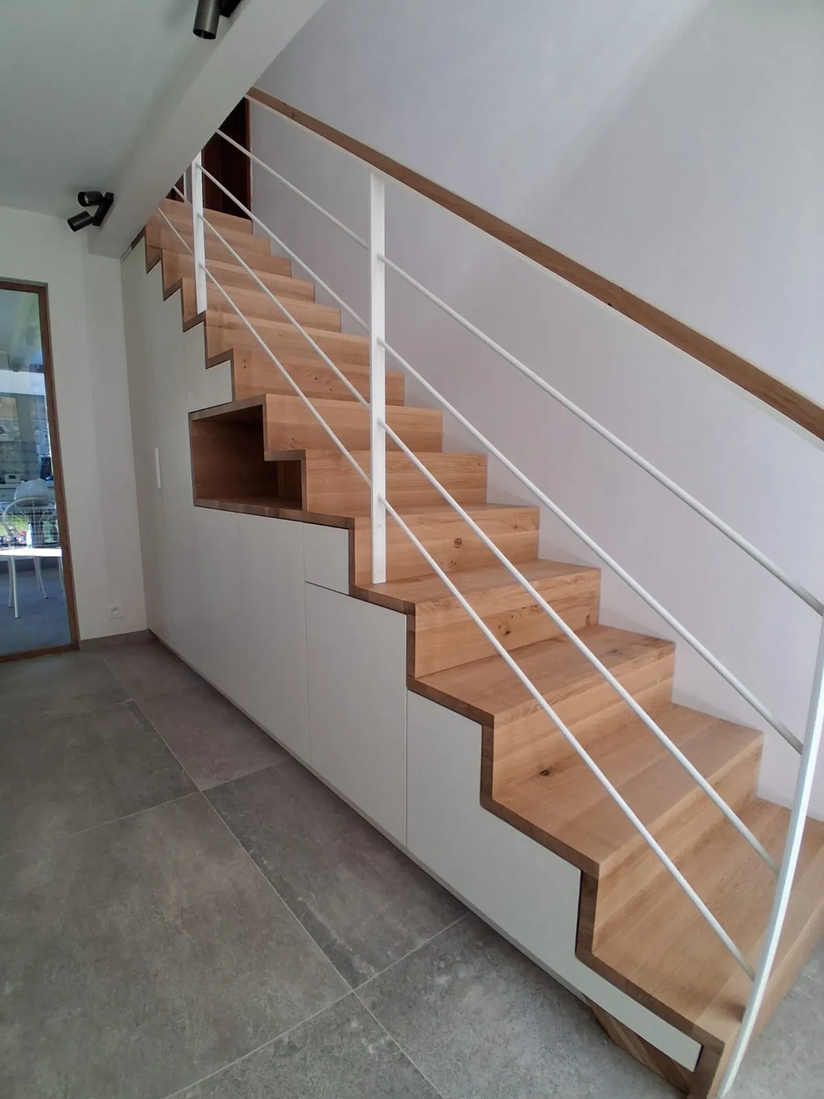 Placards blancs sur mesure sous un escalier en bois, avec niche en bois